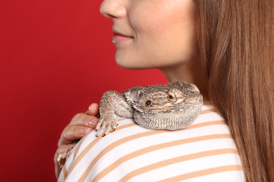 Woman with bearded lizard on red background, closeup. Exotic pet