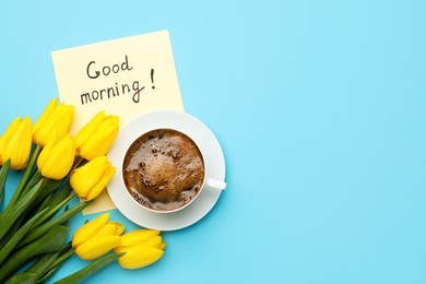 Cup of aromatic coffee, beautiful yellow tulips and Good Morning note on light blue background, flat lay. Space for text