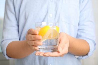 Woman holding glass of soda water with lemon slices and ice cubes, closeup