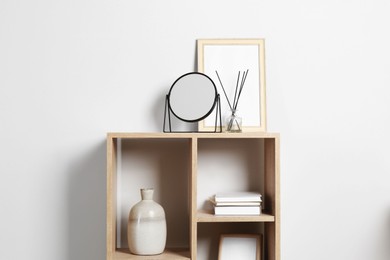 Photo of Stylish mirror, reed diffuser and picture frame on shelf near light wall. Interior design