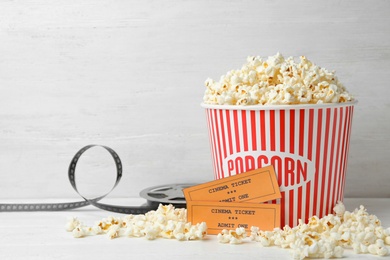 Bucket of fresh popcorn, tickets and movie reel on white wooden table, space for text. Cinema snack