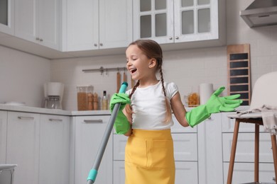 Photo of Cute little girl with mop singing while cleaning at home