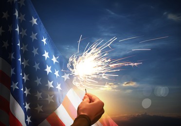 4th of July - Independence Day of USA. Woman holding burning sparkler near American flag outdoors at sunset, closeup