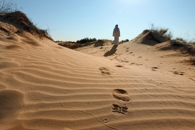 Man walking through desert, focus on footprints in sand