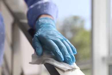 Woman in latex gloves cleaning railing with wet wipe indoors, closeup