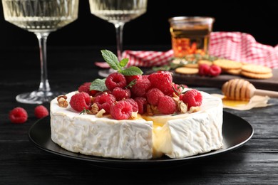 Brie cheese served with raspberries and walnuts on black wooden table