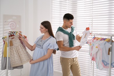 Happy pregnant woman with her husband choosing baby clothes in store. Shopping concept