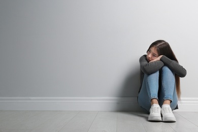 Upset teenage girl sitting on floor near wall. Space for text