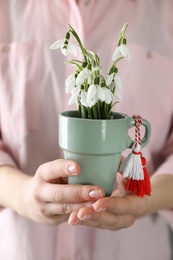 Woman holding pot with beautiful snowdrops and traditional martisor, closeup. Symbol of first spring day