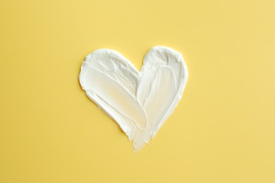 Samples of face cream in shape of heart on yellow background, top view