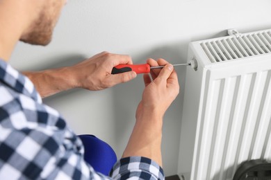Professional plumber using screwdriver while preparing heating radiator for winter season, closeup
