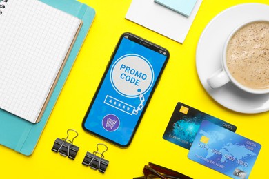 Photo of Flat lay composition of smartphone with activated promo code, credit cards and stationery on yellow table