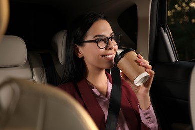 Photo of Young woman with cup of drink in modern taxi