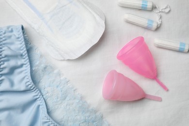 Woman's panties, menstrual pad, cups and tampons on white fabric, flat lay