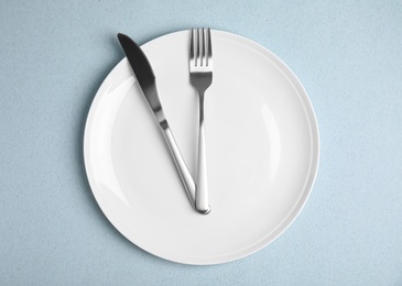 Empty plate and cutlery on light blue table, flat lay. Diet regime