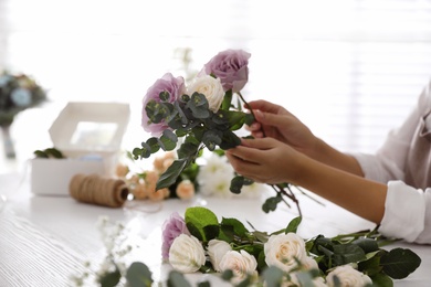 Florist making beautiful wedding bouquet at white table, closeup