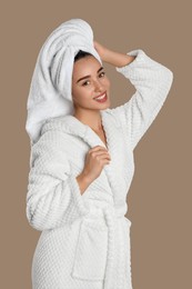 Beautiful young woman in bathrobe on brown background