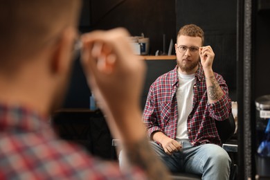 Young bearded man near mirror in barbershop