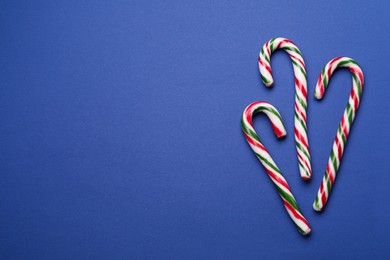 Many sweet Christmas candy canes on blue background, flat lay. Space for text