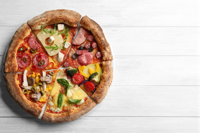 Slices of different delicious pizzas on white wooden table, top view. Space for text