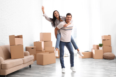 Happy couple having fun in room with cardboard boxes on moving day