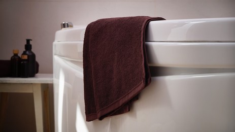 Brown soft towel on edge of bath indoors, closeup