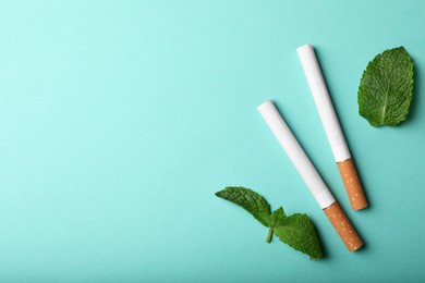 Menthol cigarettes and mint on turquoise background, flat lay. Space for text