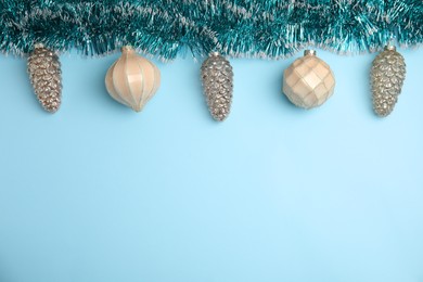 Shiny tinsel and Christmas balls on light blue background, flat lay. Space for text