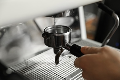 Barista cleaning portafilter at coffee machine in cafe, closeup