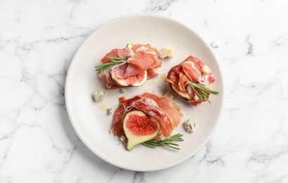 Delicious ripe figs and prosciutto served on white marble table, top view