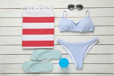 Beach towel, swimsuit, flip flops and sunglasses on white wooden background, flat lay
