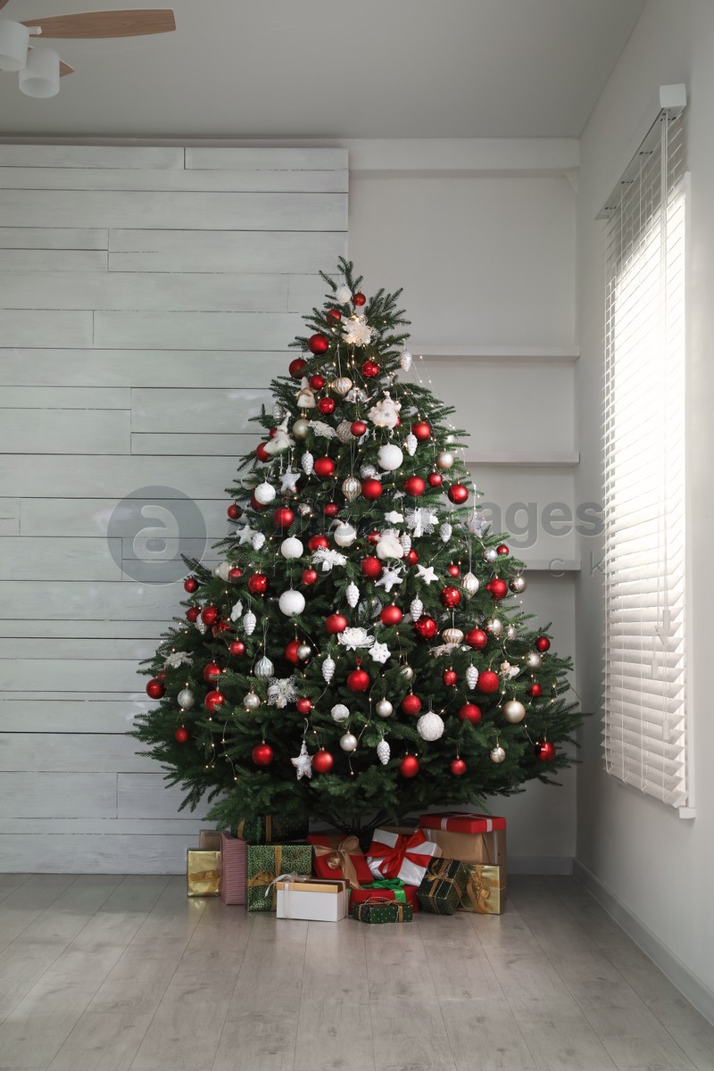 Beautifully decorated Christmas tree and gifts near window indoors