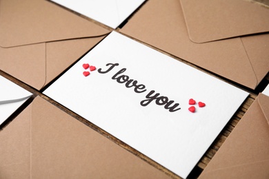 Sheet of paper with phrase I Love You, envelopes and heart shaped sprinkles on wooden table, closeup