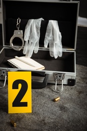 Crime scene marker and open case with police equipment on grey stone table