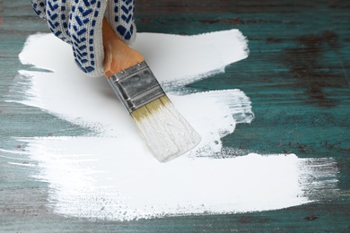 Person painting teal wooden surface white, closeup
