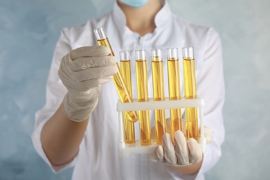 Doctor holding test tubes with urine samples for analysis on light blue background, closeup