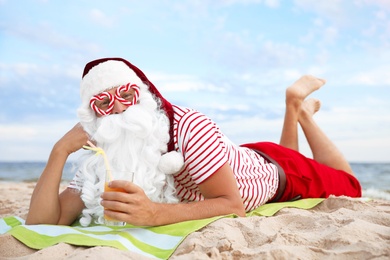 Santa Claus in party glasses with cocktail relaxing on beach. Christmas vacation