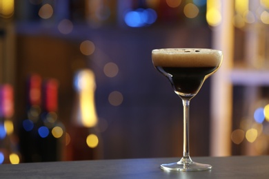 Glass of Espresso Martini on counter in bar, space for text. Alcohol cocktail
