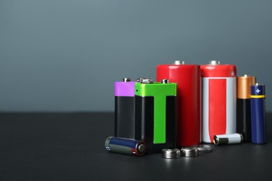 Different types of batteries on black table against grey background, space for text