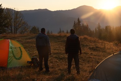 Tourists enjoying sunrise near camping tents in mountains, back view