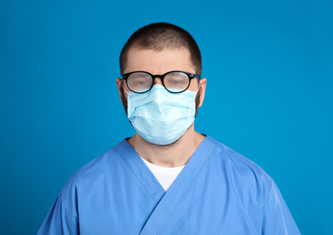 Doctor with foggy glasses caused by wearing disposable mask on blue background. Protective measure during coronavirus pandemic