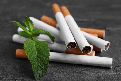 Menthol cigarettes and mint on grey table, closeup