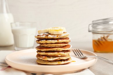 Plate of banana pancakes with honey and powdered sugar served on table