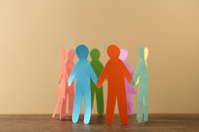 Photo of Many different paper human figures standing in circle on wooden table against beige background. Diversity and inclusion concept