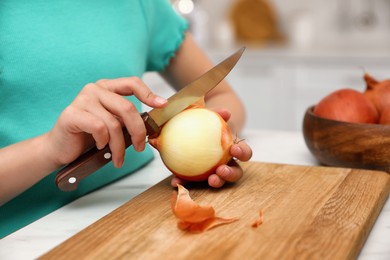 Little girl peeling onion at table in kitchen, closeup. Preparing vegetable