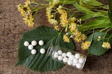 Bottle of homeopathic remedy, linden flowers and leaves on wooden background, flat lay