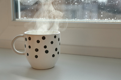 Cup of hot drink near window on rainy day.  Space for text