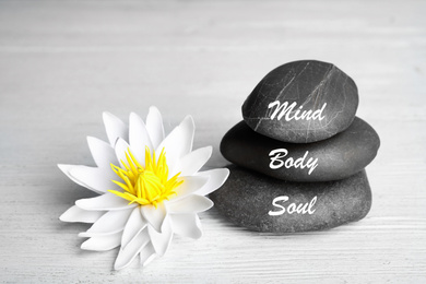 Stones with words Mind, Body, Soul and lotus flower on white wooden table. Zen lifestyle