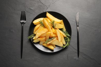 Photo of Served tasty baked potato wedges and rosemary on black table, flat lay
