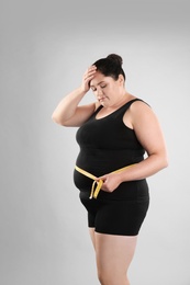 Fat woman with measuring tape on grey background. Weight loss